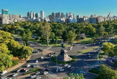 Aerial view of a central monument surrounded by lush green parks, busy avenues, and the urban skyline of Buenos Aires