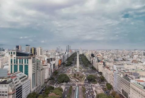 Busy street scene in downtown Buenos Aires showing pedestrians, cars, and a local bus, with the towering white Obelisk at the end of the avenue