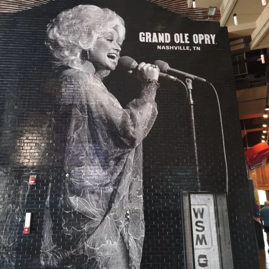 A large black brick mural featuring a black and white portrait of Dolly Parton singing into a microphone at the Grand Ole Opry in Nashville, Tennessee