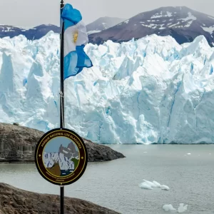 Los Glaciares National Park sign with the Argentinian flag in the foreground and the massive ice walls of the Perito Moreno Glacier in the background.