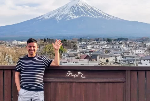 Man waving in front of the snow-capped Mount Fuji and town view from a wooden viewpoint in Fujikawaguchiko, Japan.
