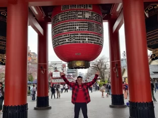 Man posing with open arms beneath the giant red lantern at Senso-ji temple in Asakusa, Tokyo, Japan