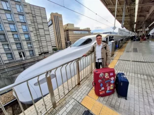 Passenger standing with luggage on the train station platform next to a white Shinkansen N700 bullet train in Japan.