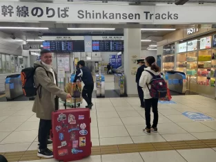 Traveler with luggage standing in front of the Shinkansen bullet train ticket gates and departure boards at a Japan train station.